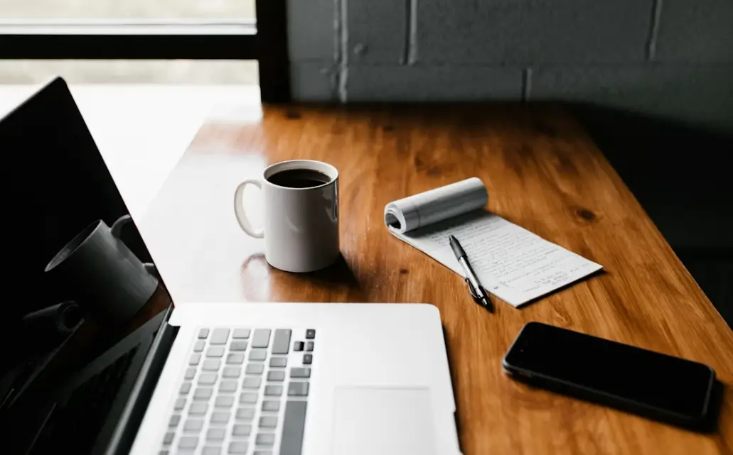 pc posé sur un bureau à côté d'un mug de café, d'un bloc-notes et d'un smartphone